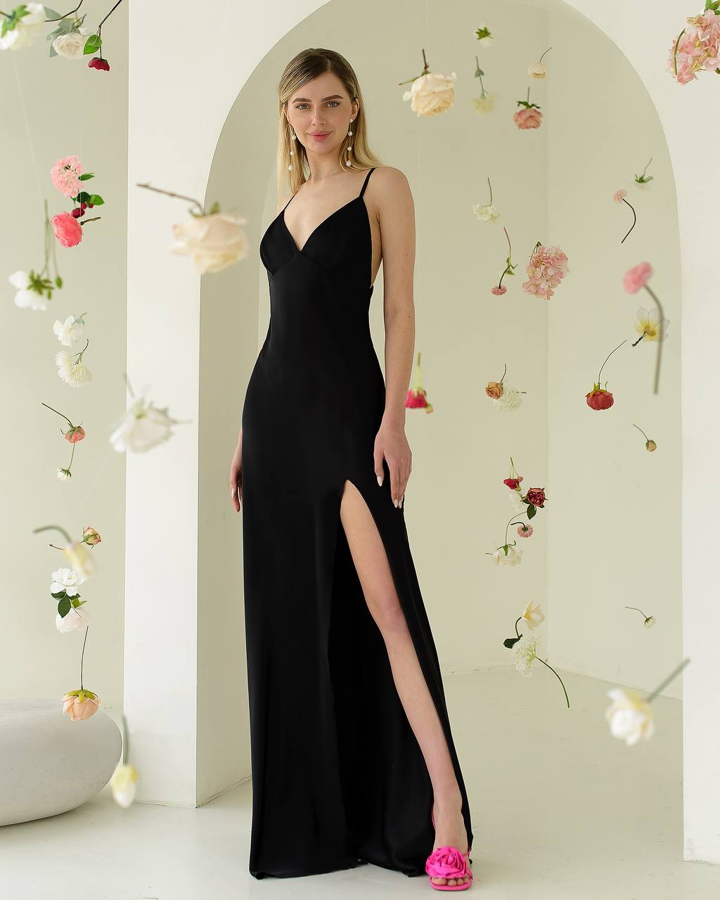 Woman in a black dress with a high slit standing in front of a floral arch.