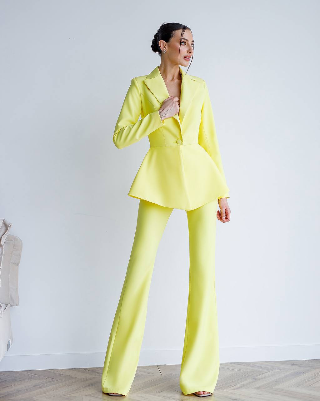 Woman wearing a bright yellow suit standing against a white wall.