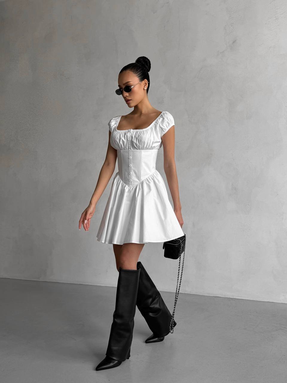 Woman wearing a white dress and black knee-high boots against a gray background