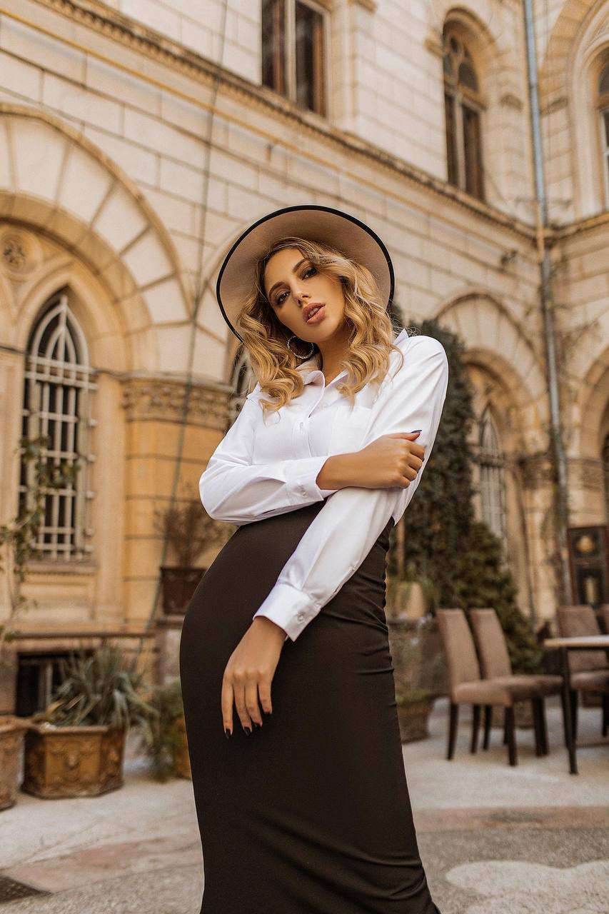 Woman in a white shirt and dark skirt standing in front of an architectural building.