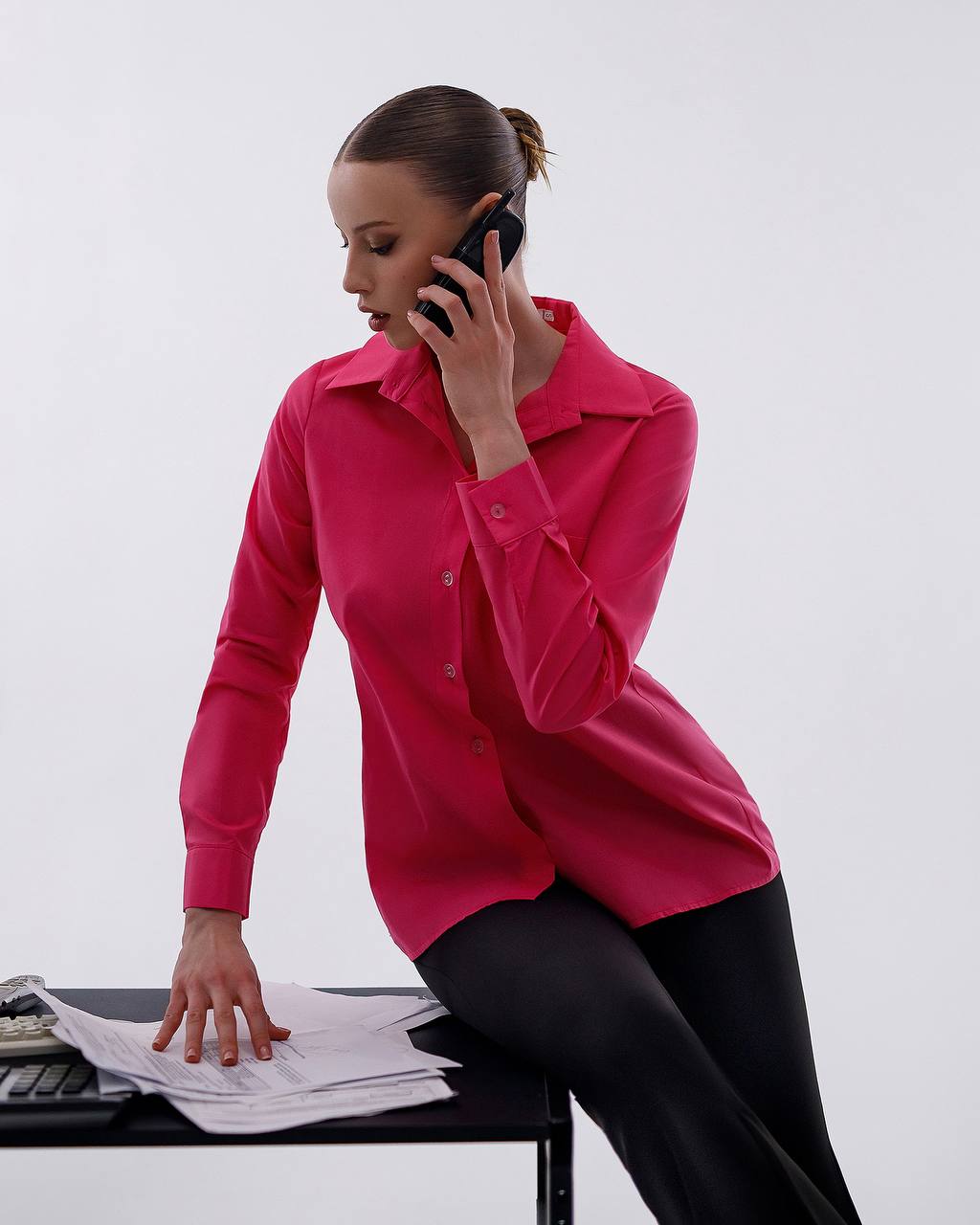 Woman in a pink shirt talking on a phone with papers in front of her