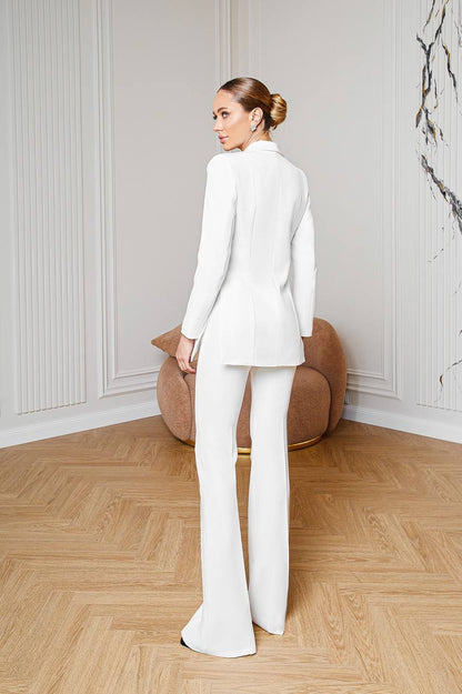 Woman in a white suit standing in a room with wooden flooring and a decorative wall.