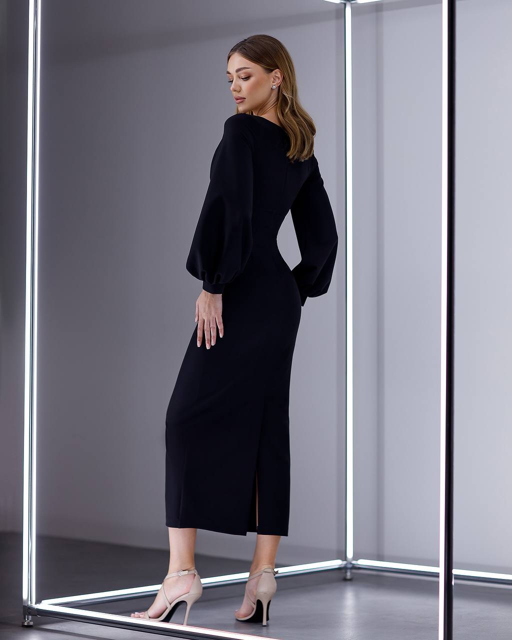 Woman wearing a black dress in a modern fitting room with reflective floor.