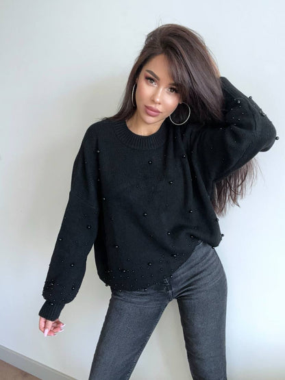Woman wearing a black sweater with small embellishments against a white wall