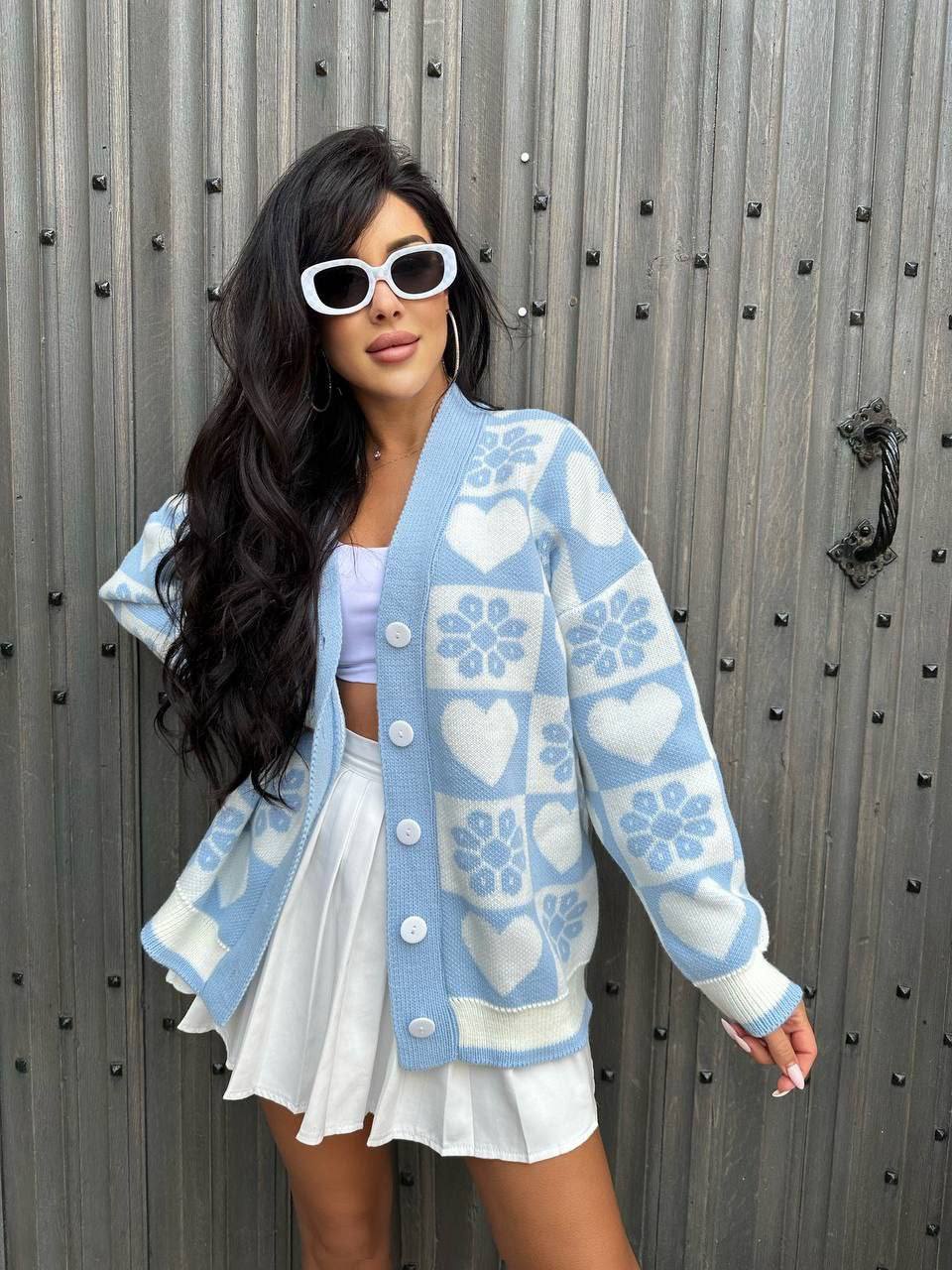 Woman wearing a blue patterned cardigan in front of a metallic wall.