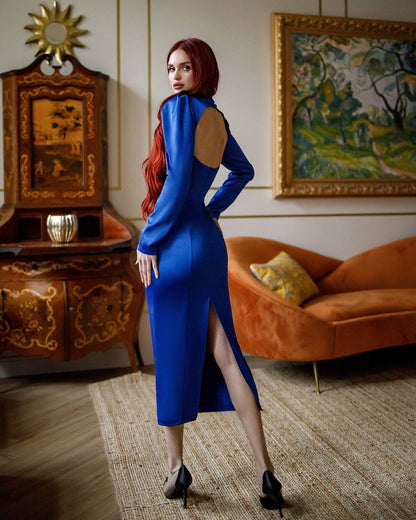 Woman in a blue dress standing in an elegant room with a painting and furniture.