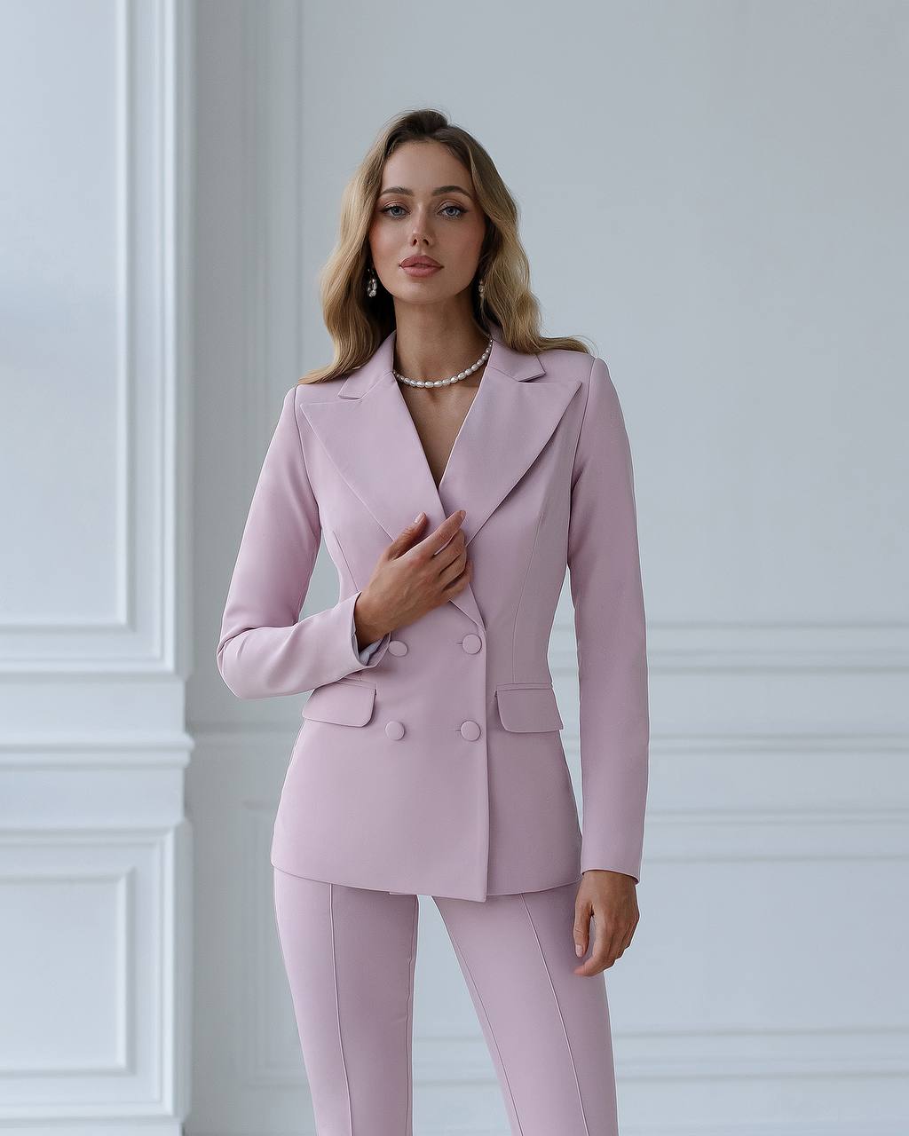 Woman wearing a pink suit standing against a white wall