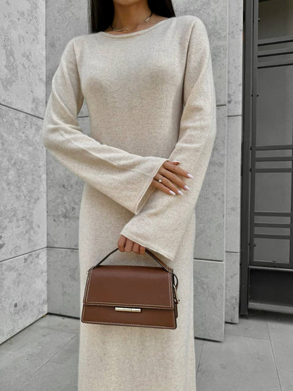 Person wearing a beige sweater dress holding a brown handbag against a neutral background