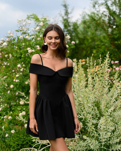 Woman wearing a black dress standing in a garden with greenery and flowers.