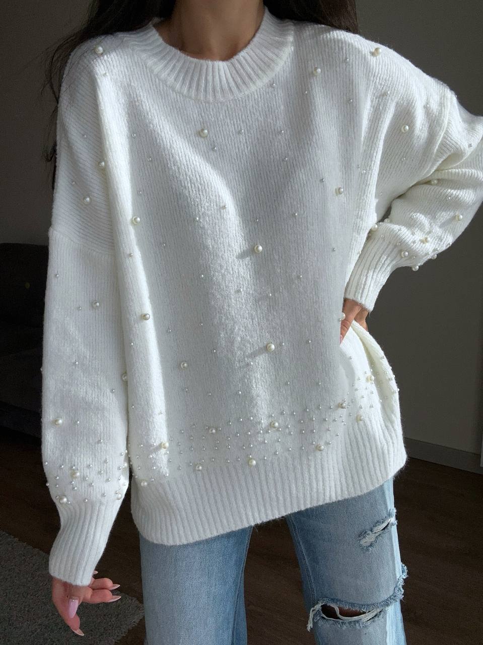 White sweater with pearl embellishments worn by a person, with a blurred background.