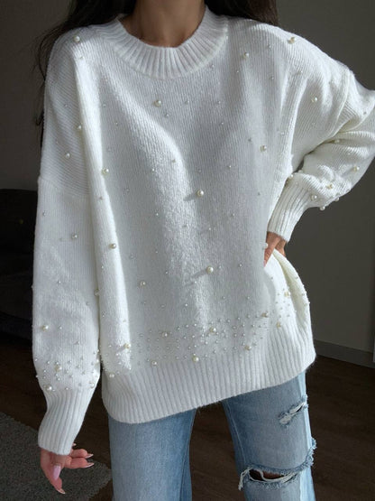 White sweater with pearl embellishments worn by a person, with a blurred background.