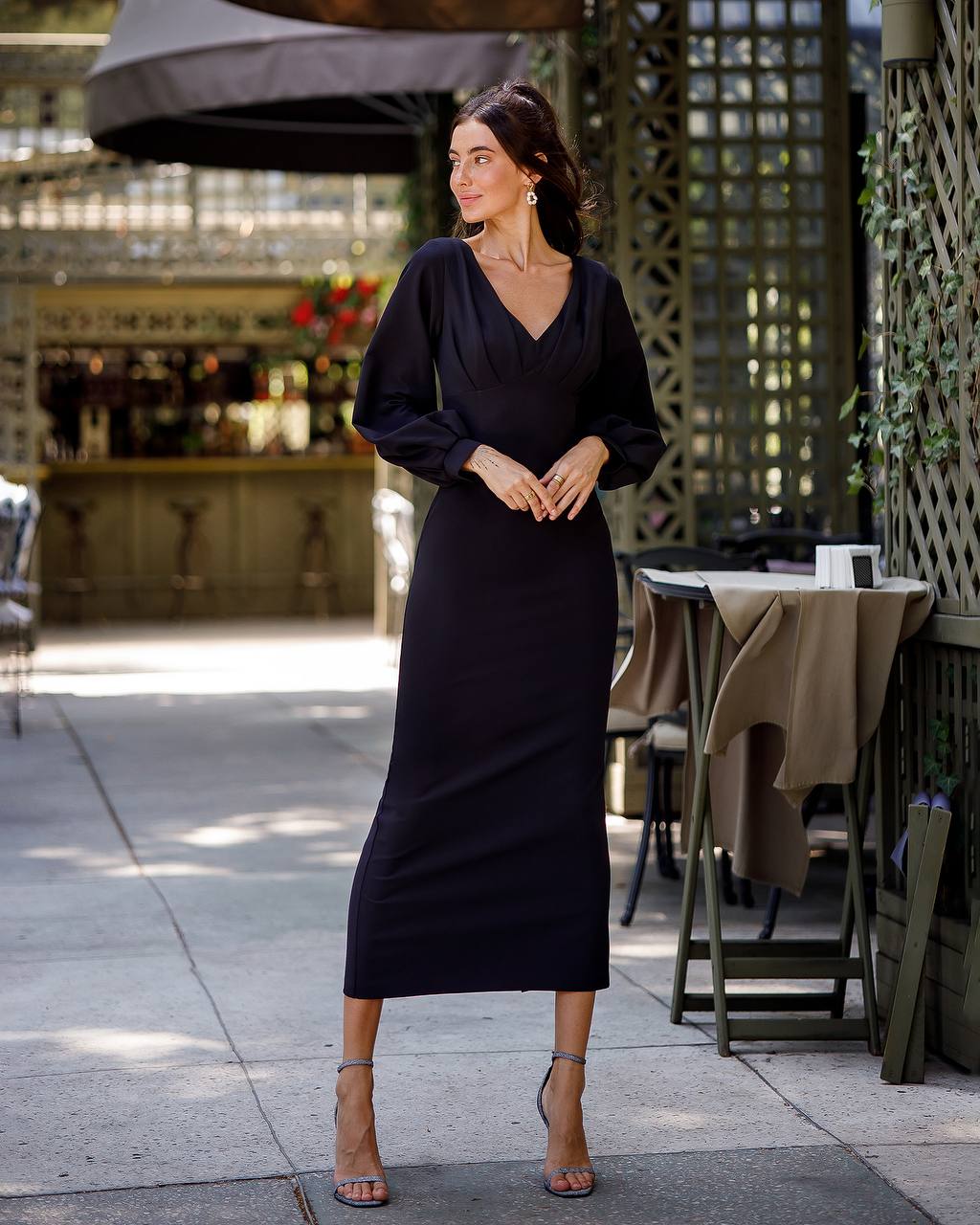 Woman in a black dress standing outdoors near a bar area.