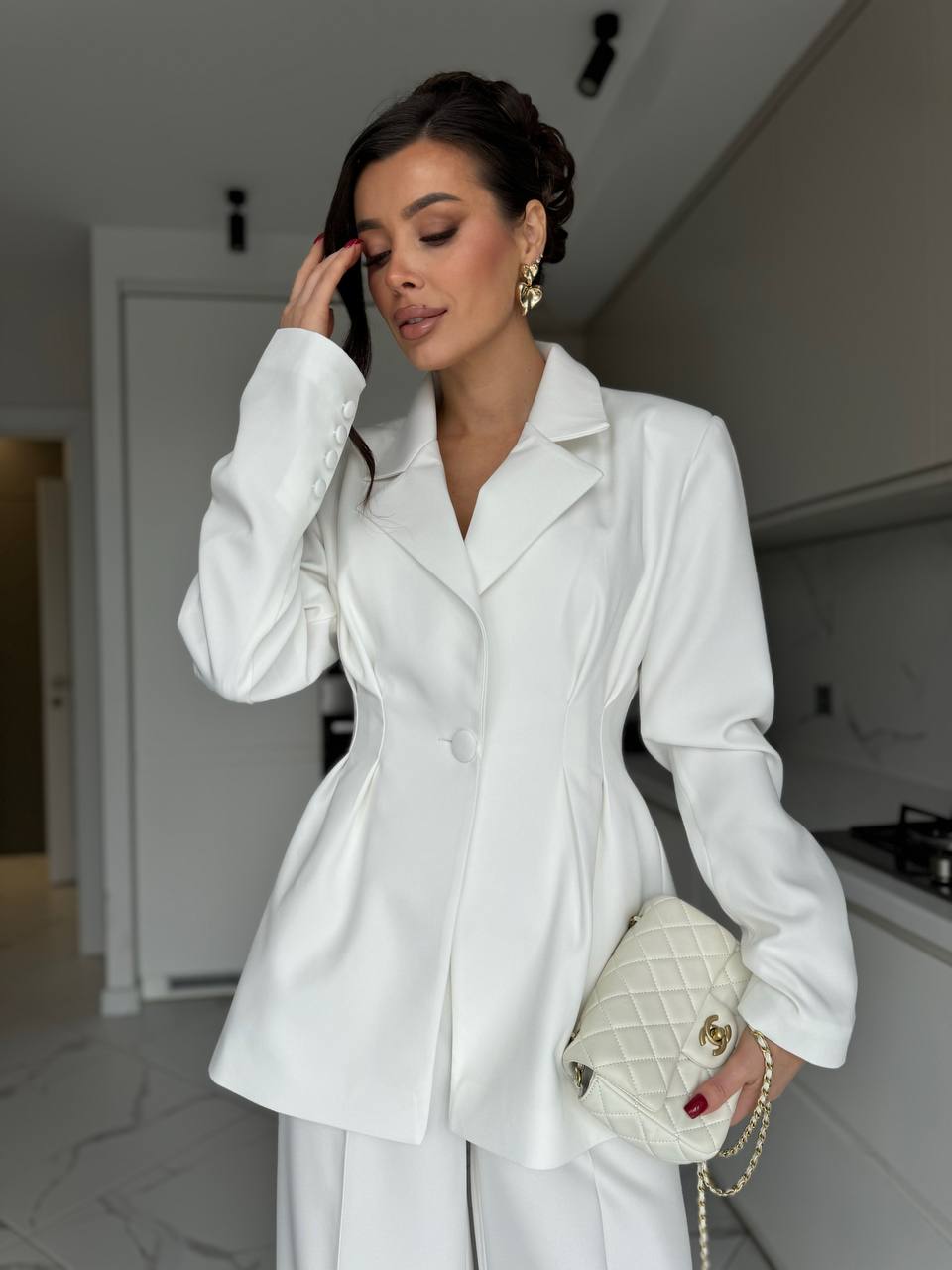 Woman in a white outfit holding a white handbag in a kitchen setting
