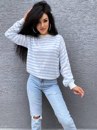 Woman wearing a striped sweater and jeans against a gray wall