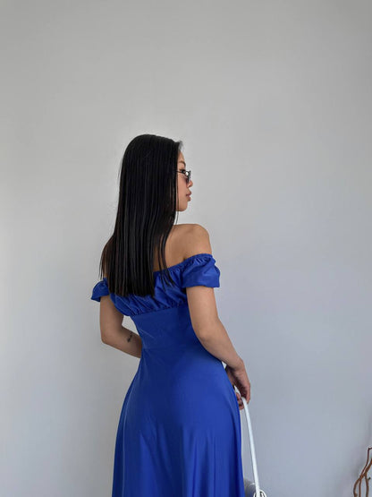 Woman in a blue off-shoulder dress standing against a plain background
