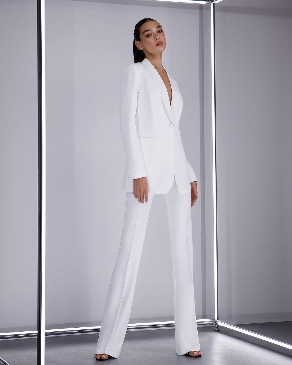 Woman wearing a white suit standing in a futuristic, metallic room.