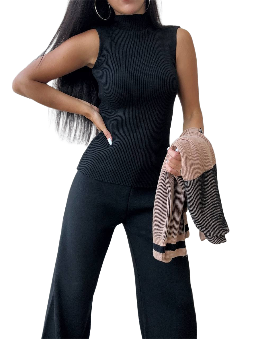 Woman wearing a black sleeveless top and pants holding a jacket on a white background