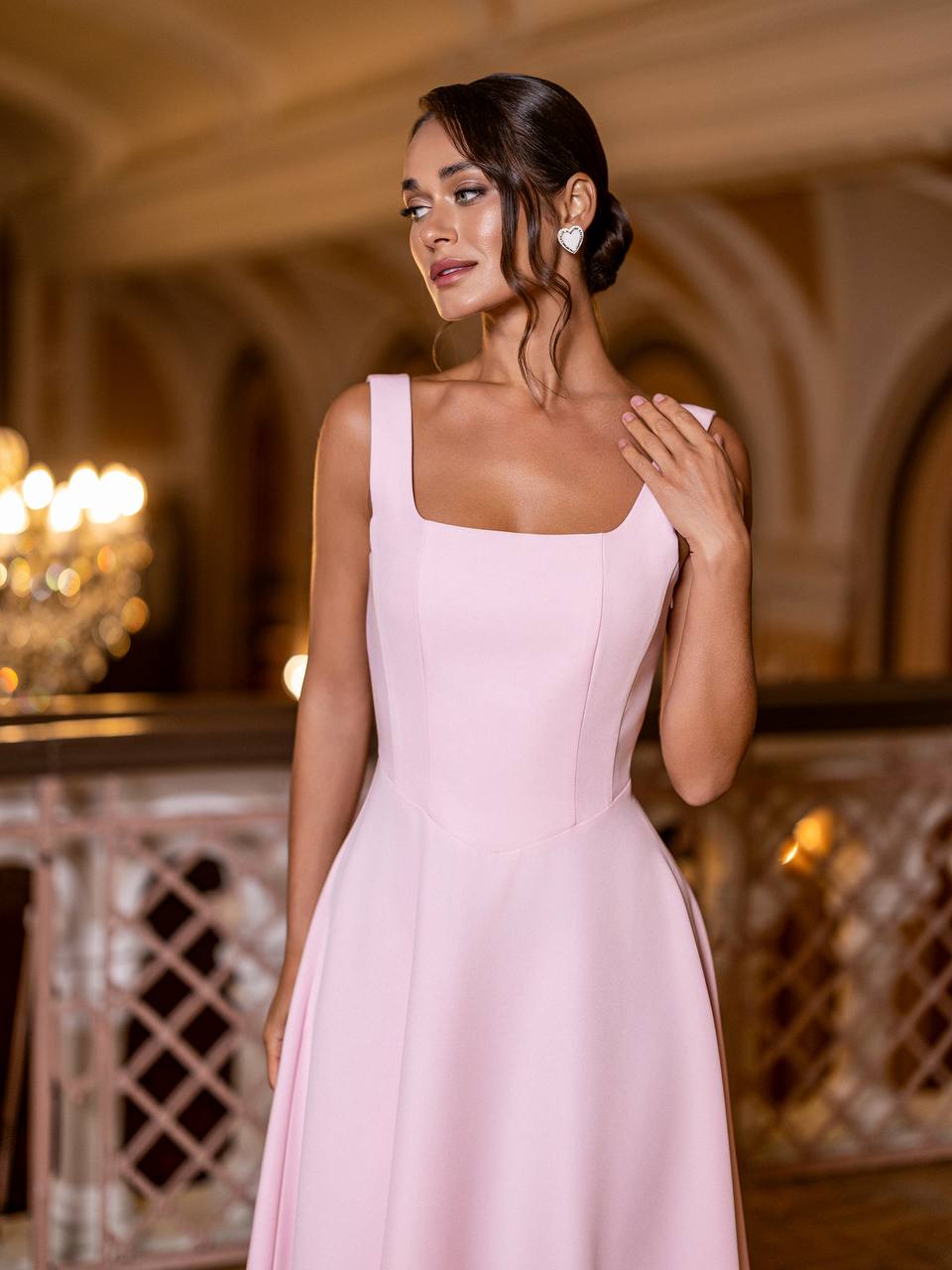Woman in a pink dress standing in an elegant indoor setting with chandeliers.