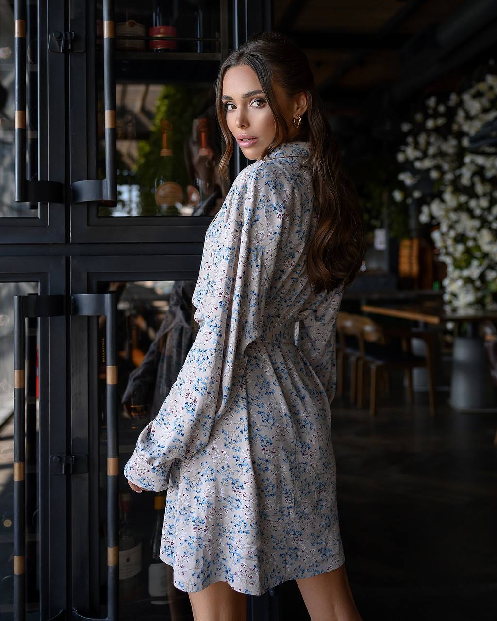 Woman in a floral dress standing in a dimly lit room with decorative elements.