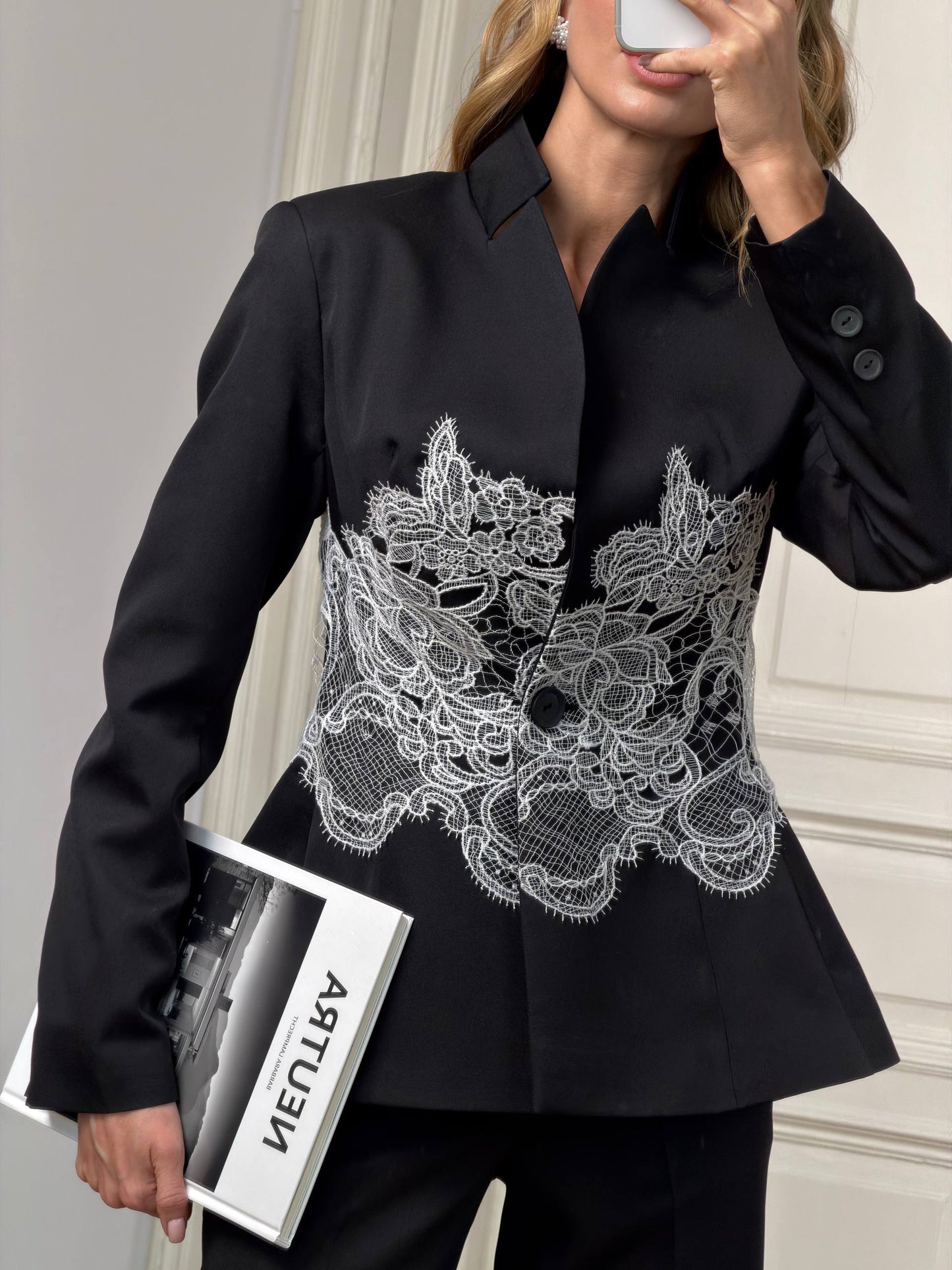 Black blazer with white lace detailing worn by a person, holding a magazine.