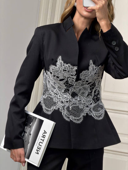 Black blazer with white lace detailing worn by a person, holding a magazine.