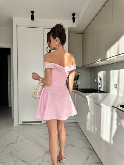 Woman in a pink off-shoulder dress standing in a modern kitchen.