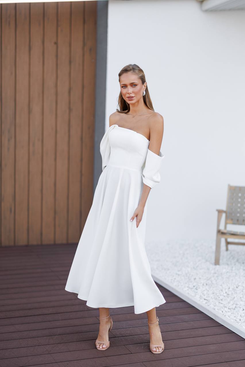 Woman wearing a white one-shoulder dress on a wooden deck.
