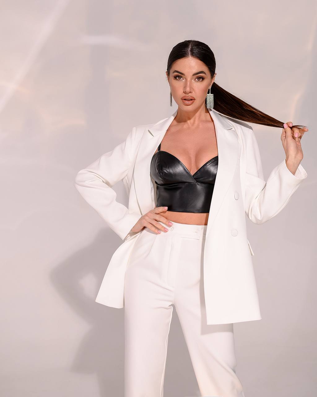 Woman in a white suit with a black leather top against a light background