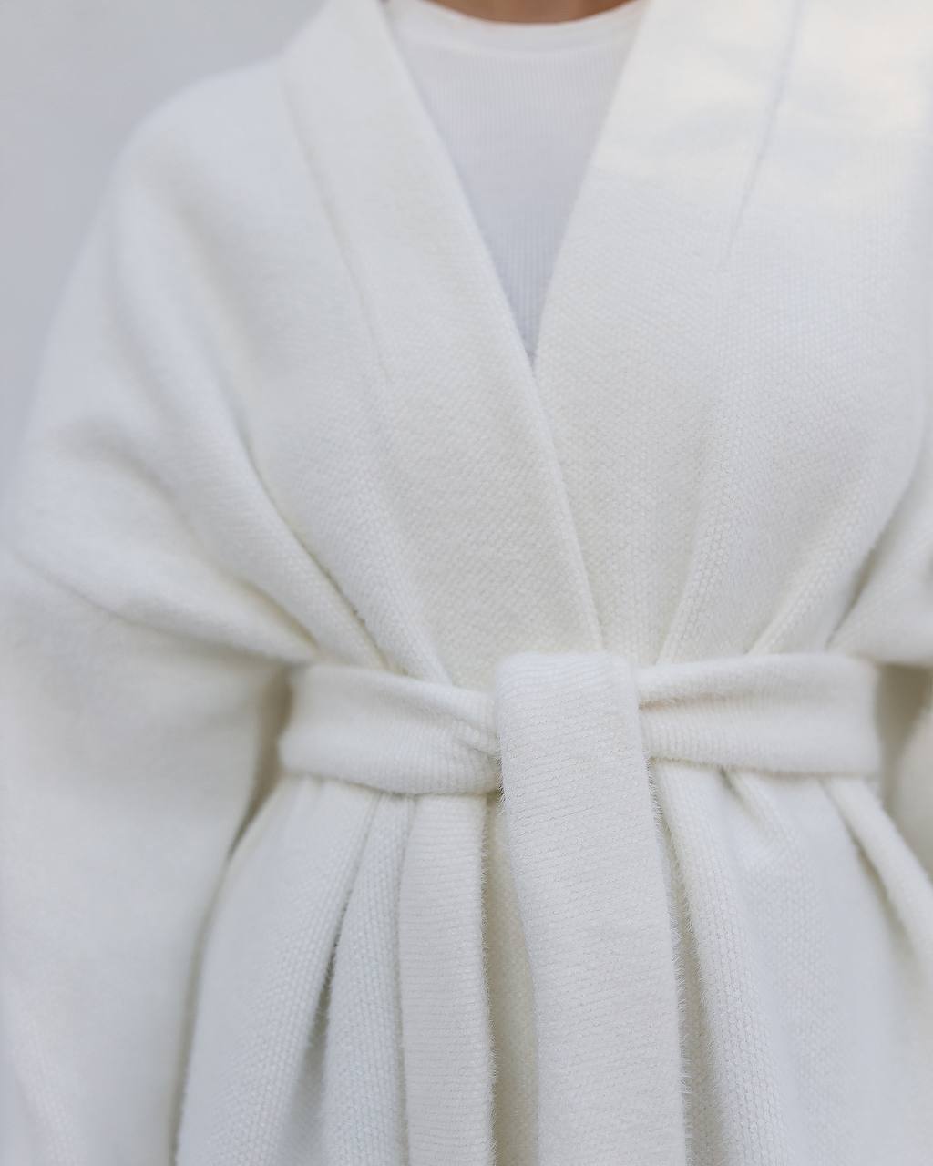 Close-up of a white robe with a belt on a plain background