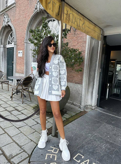 Woman in a white outfit with heart patterns standing on a sidewalk in an urban setting.