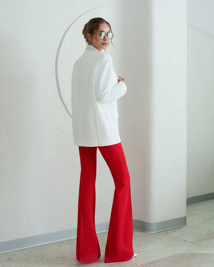 Person wearing a white top and red pants standing against a plain wall.