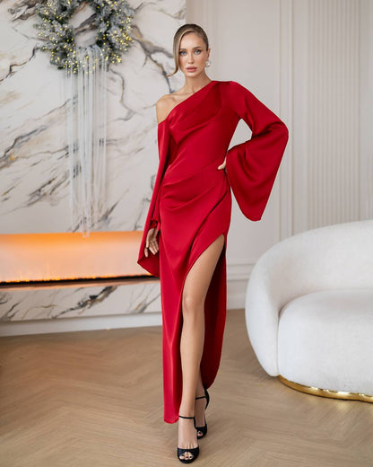 Woman in a red one-shoulder dress with a high slit standing in an elegant interior setting.