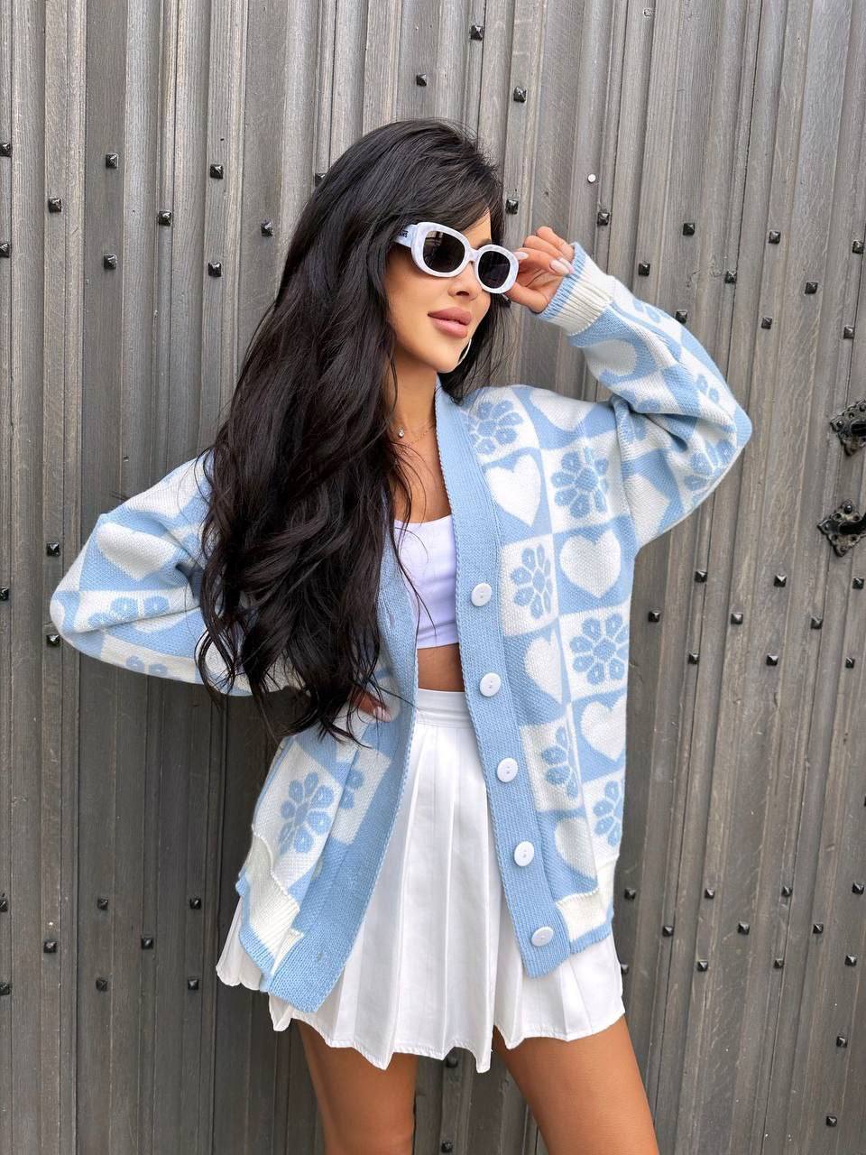 Woman wearing a blue and white patterned cardigan over a white outfit against a metallic background