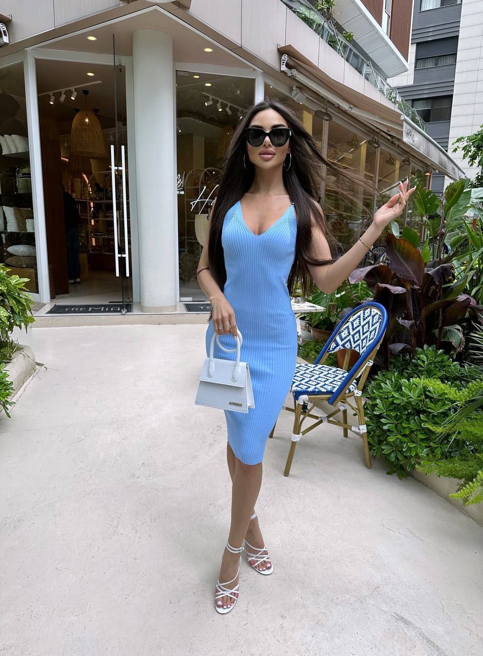 Woman in a blue dress standing outdoors with a building and chair in the background