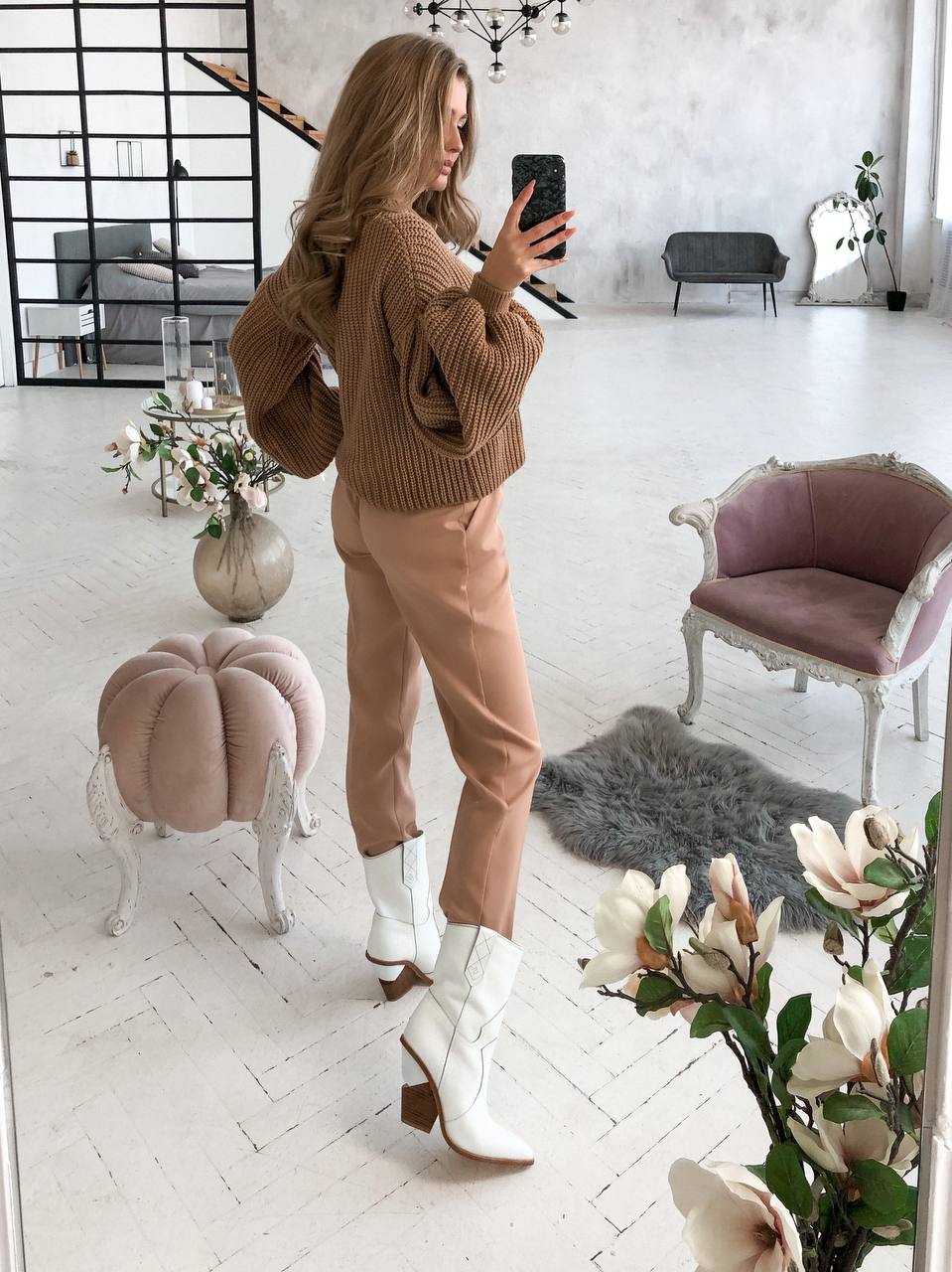 Woman taking a mirror selfie in a stylish room with decor elements.