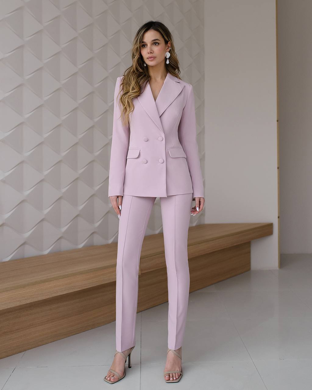 Woman wearing a light purple suit standing against a textured wall.
