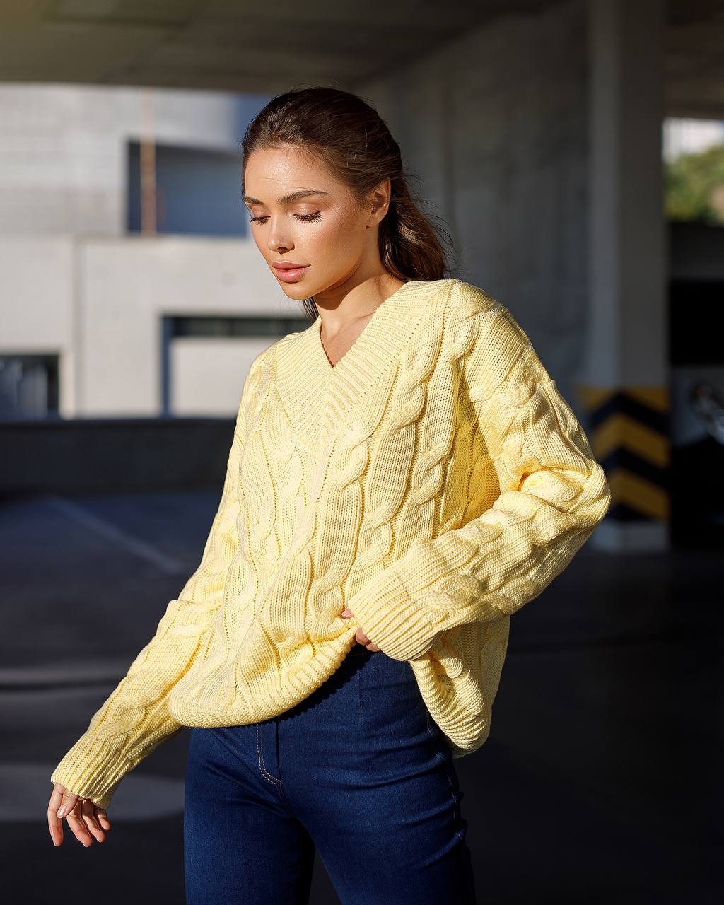 Woman wearing a yellow cable knit sweater and blue jeans standing outdoors.