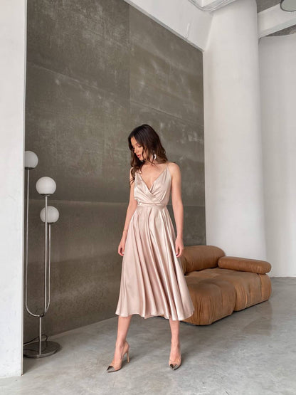 Woman in a beige dress standing in a modern room with a brown sofa and gray walls.