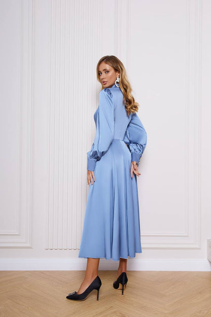 Woman wearing a blue dress standing against a white wall.