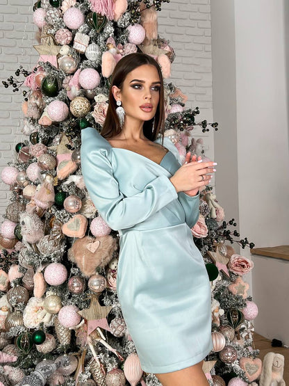 Woman in a light blue dress standing in front of a decorated Christmas tree with pink and gold ornaments.