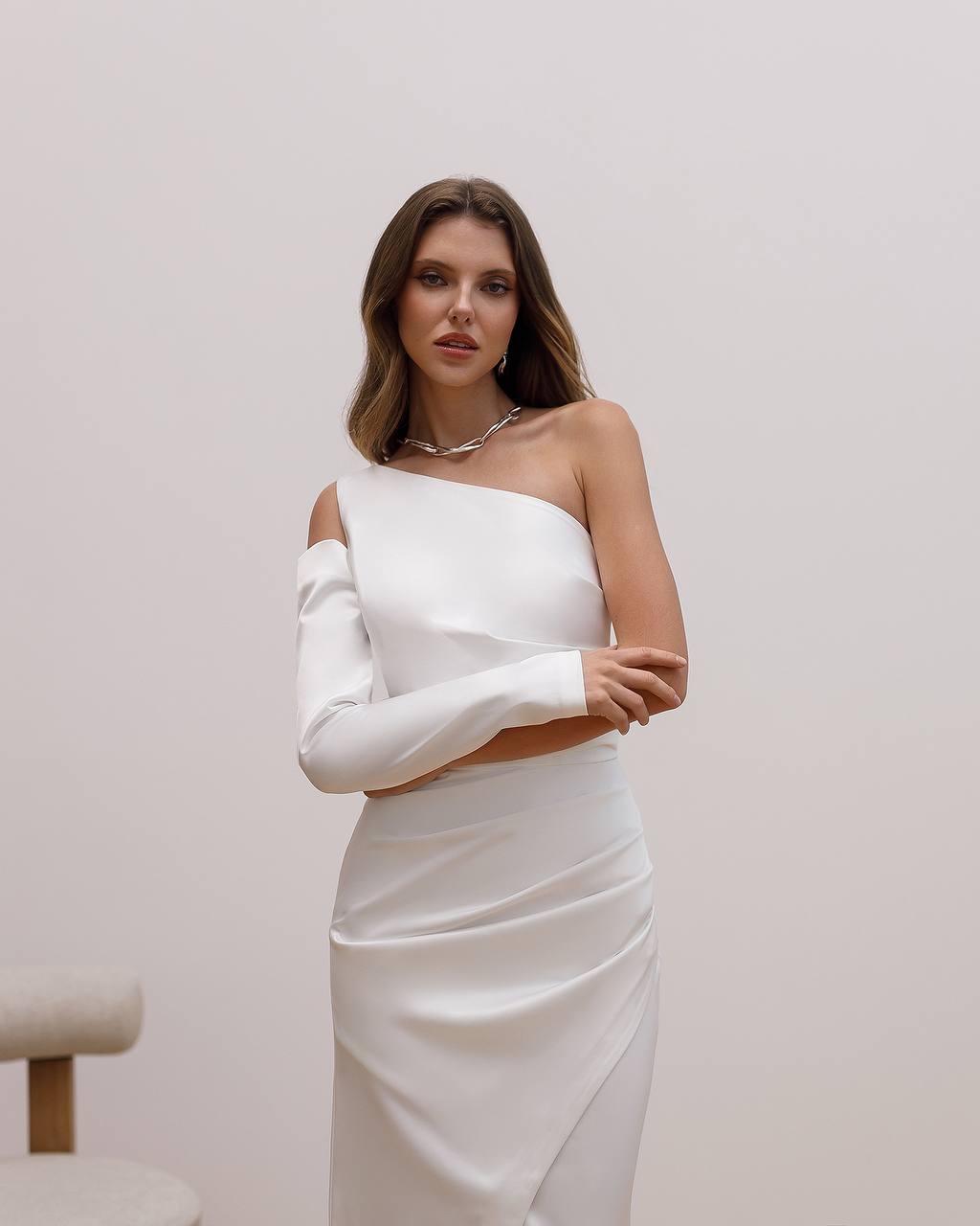 Woman wearing a white one-shoulder dress against a plain background