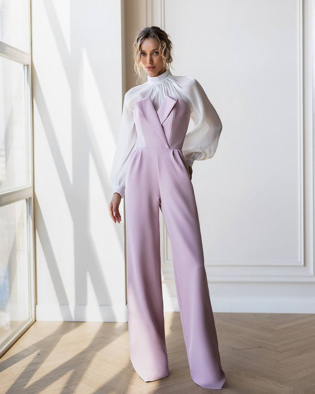 Woman wearing a lavender jumpsuit with a white blouse in a bright room.