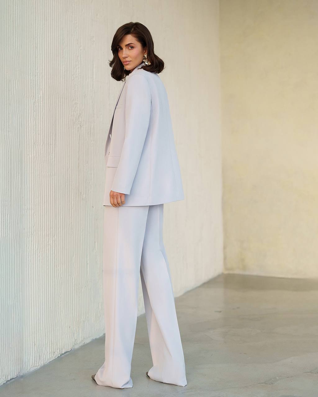 Woman wearing a light gray suit standing against a neutral background