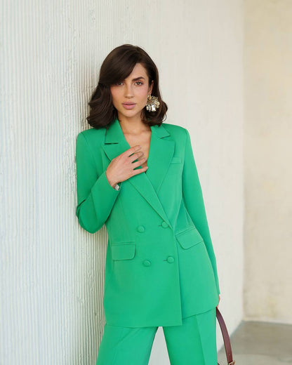 Woman wearing a green suit standing against a neutral wall.
