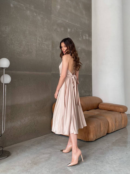 Woman in a beige dress standing in a modern room with a brown sofa and gray walls.