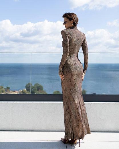 Woman in a patterned dress standing on a balcony with a scenic view of water and sky.