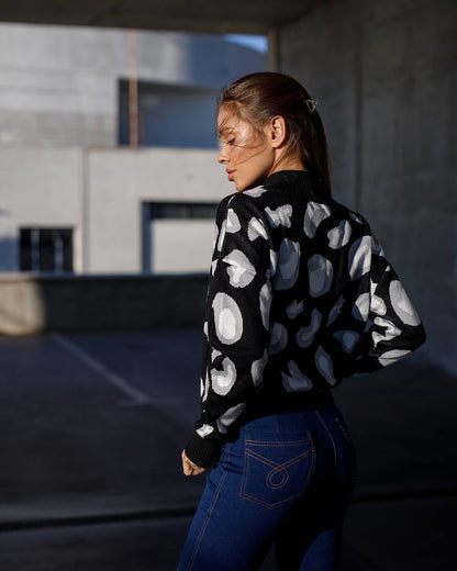 Woman wearing a black sweater with white patterns and blue jeans, standing outdoors.