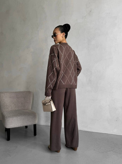 Person wearing a brown outfit with a geometric pattern, standing against a plain wall with a chair.