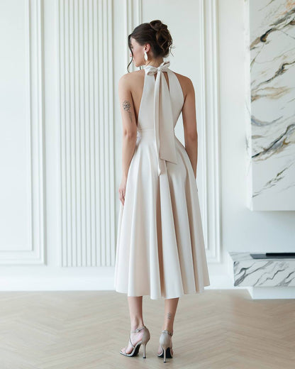 Woman wearing a white halter neck dress with a bow detail in a modern interior setting.