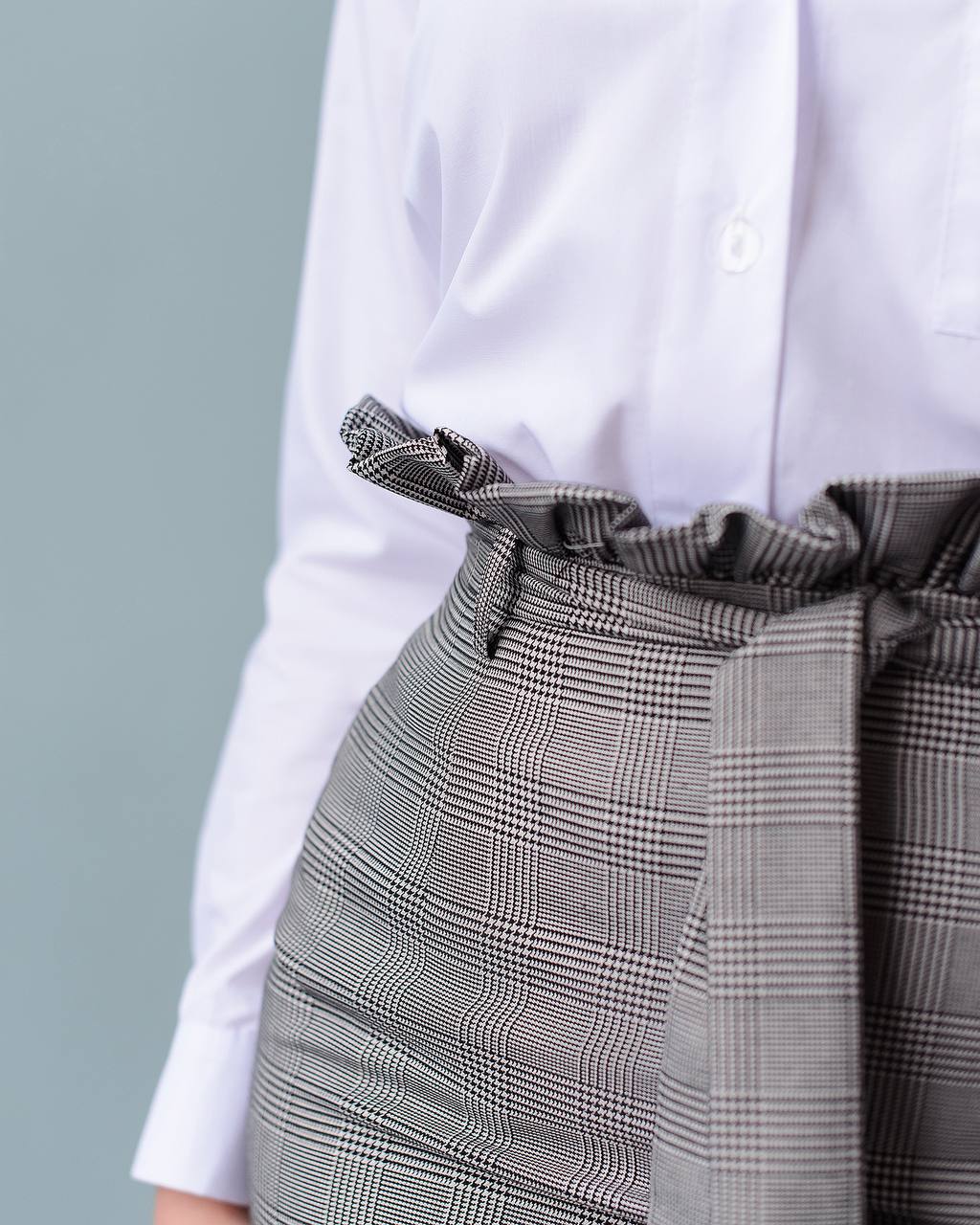Person wearing a white shirt and gray checkered skirt with a belt against a light gray background